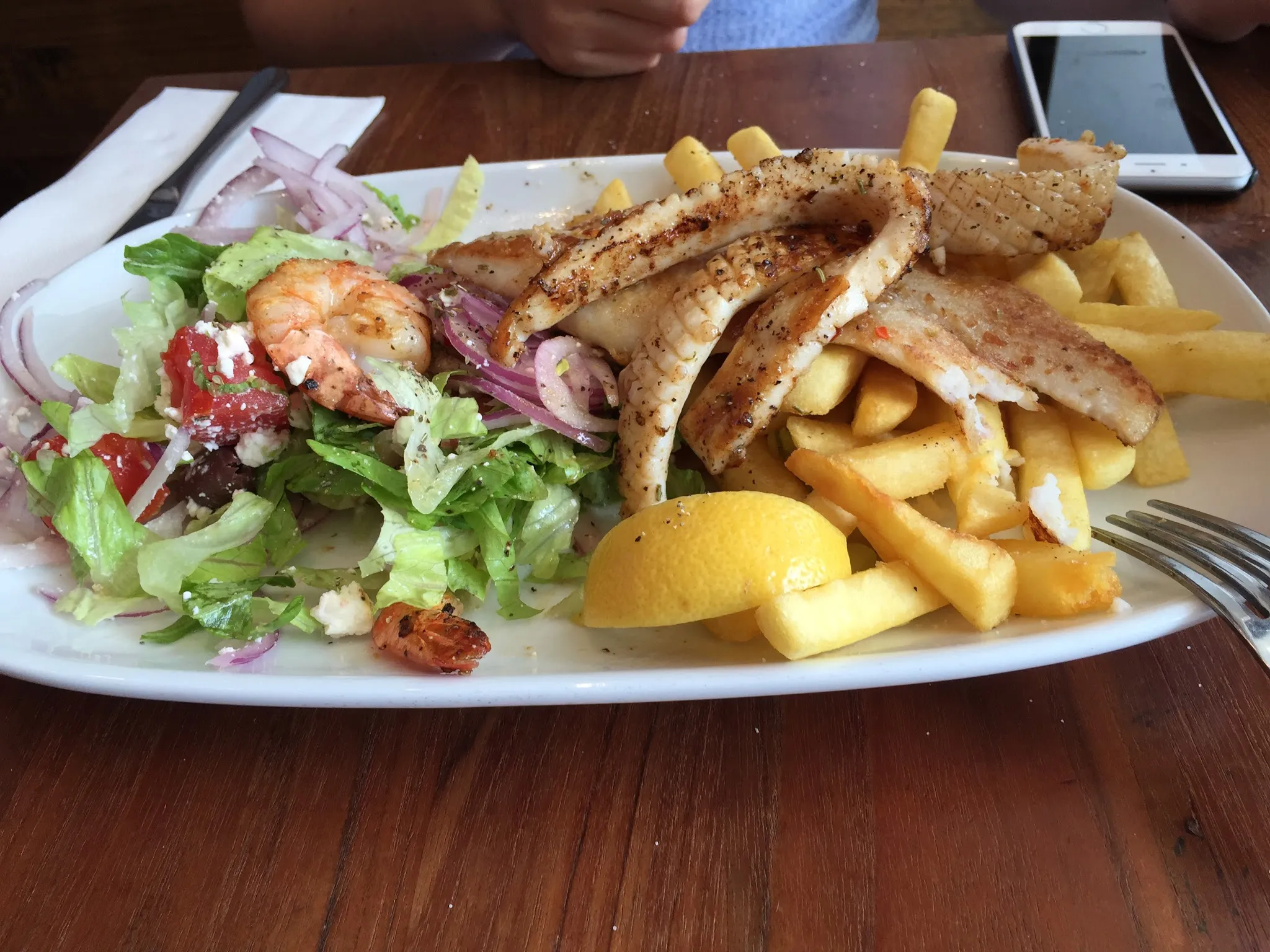 Grilled fish and squid with chips, salad and lemon wedge on white plate