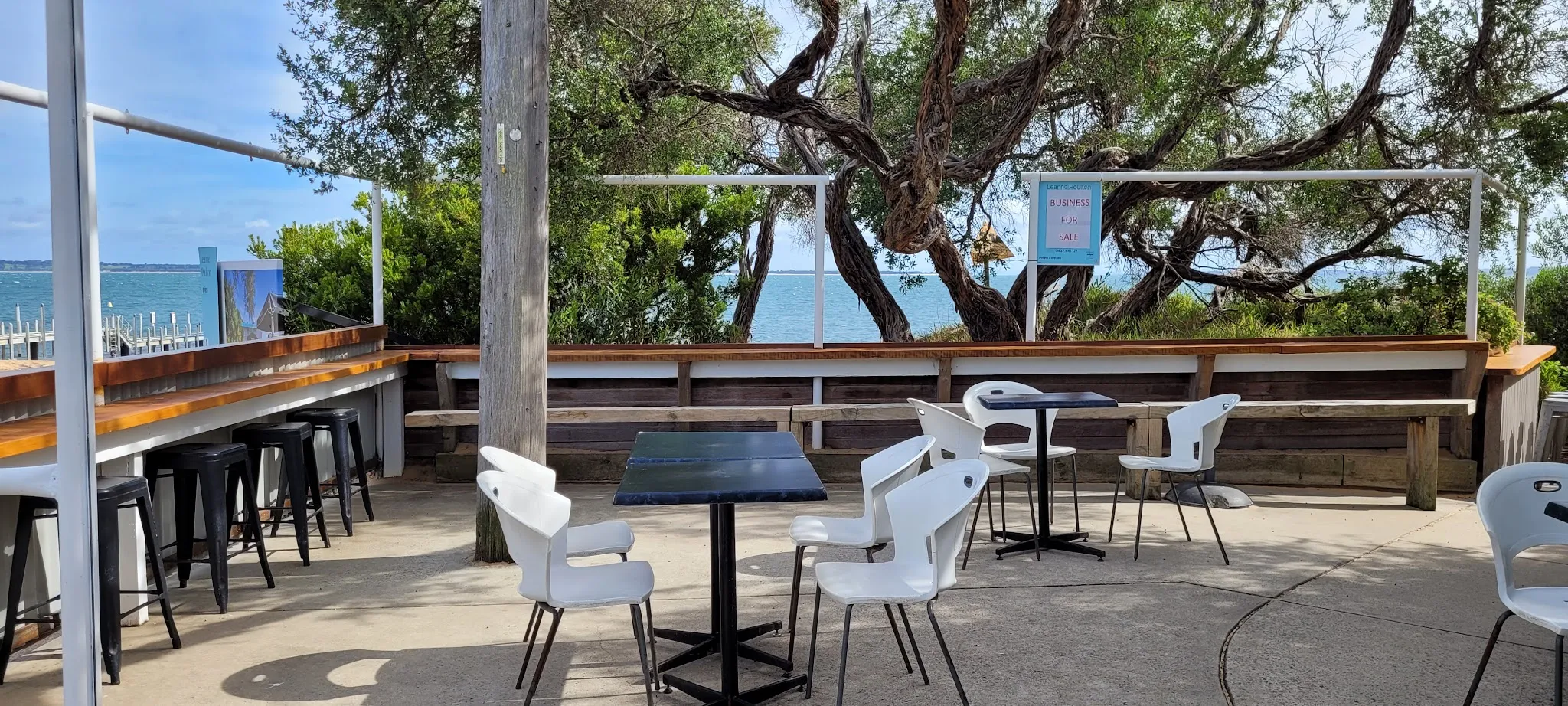 Boatramp Cafe outdoor deck with white chairs, bar counter and bay glimpsed through trees
