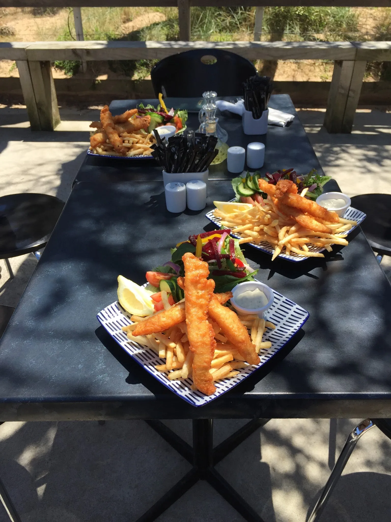 Three baskets of battered flathead tails with chips and salad at outdoor table