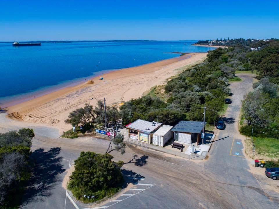 Aerial view of Boatramp Cafe beside a sweeping golden beach with vivid blue bay